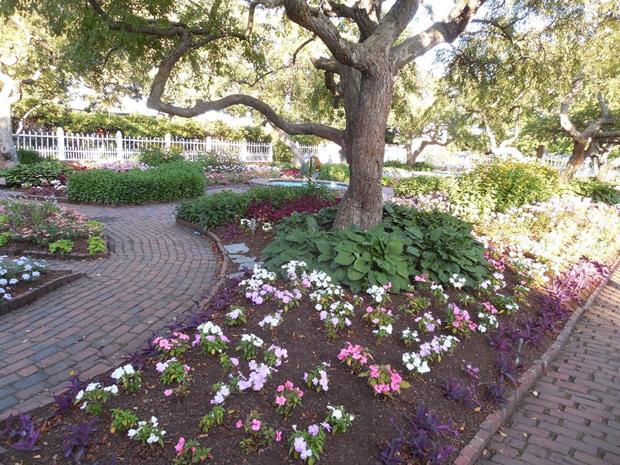 Garden with brick pathway and colorful flowers under large oak trees